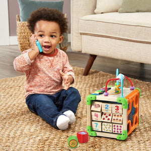Toddler on the phone beside the LeapFrog Wooden Activity Cube