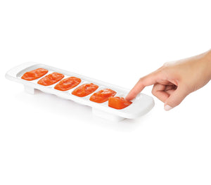 OXO Tot freezer tray holding six cubes of orange baby food, one being pushed out