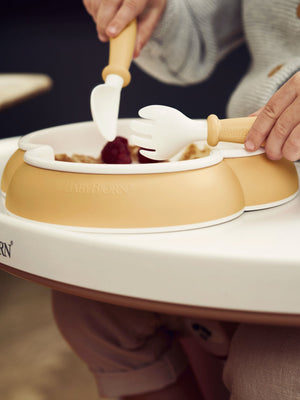 Child self-feeding from the BabyBjorn Baby Plate in Powder Yellow