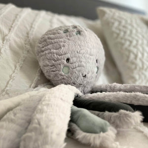 Inky the Grey Octopus plush on a bed